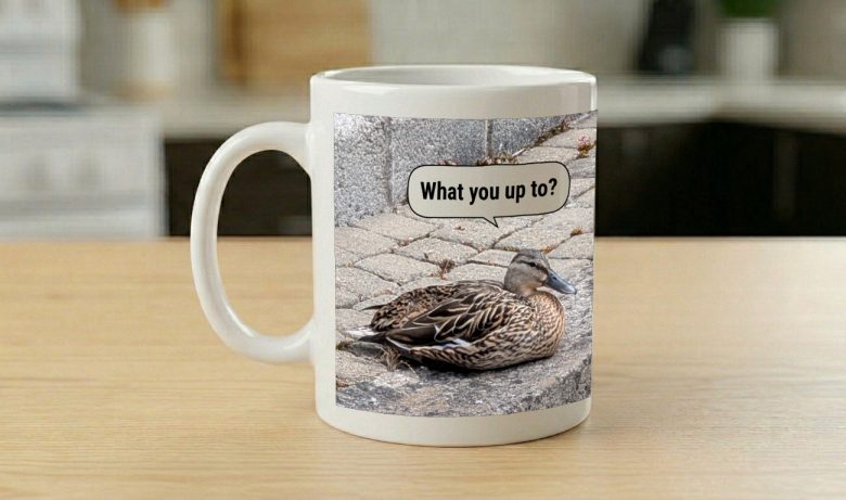 Mug printed with a duck on a cobbled path, a speech bubble asking "What you up to?"
